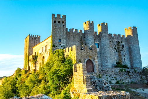 Kasteel van Óbidos in Portugal met hoge stenen muren, middeleeuwse torens en historische gebouwen onder een heldere blauwe lucht.